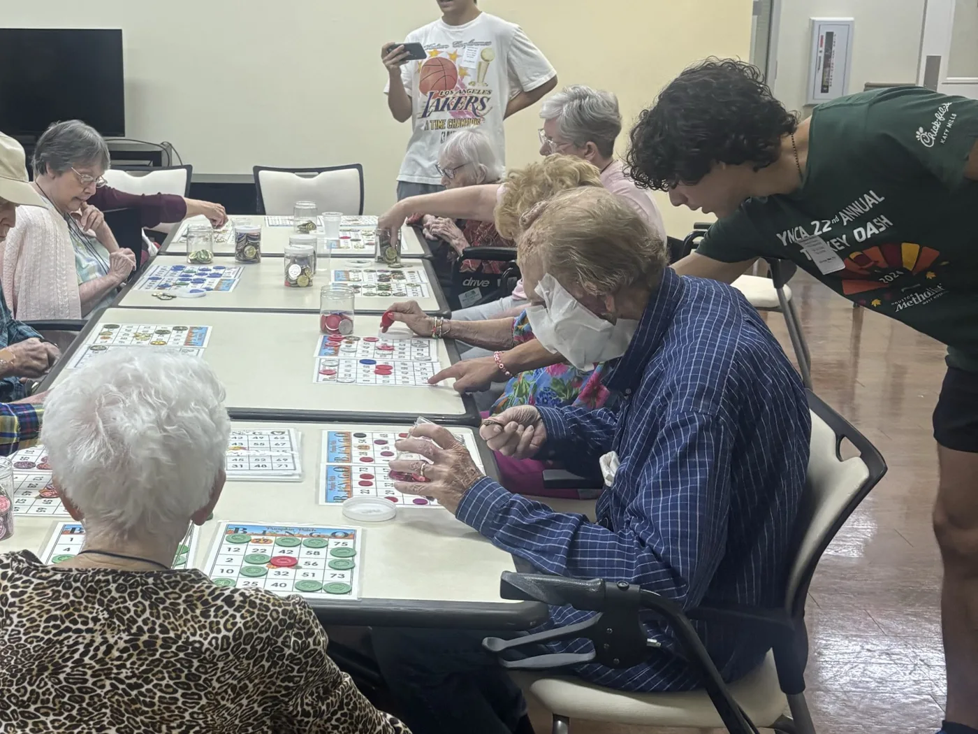 A volunteer leans in to help a resident mark his bingo card while other residents play
